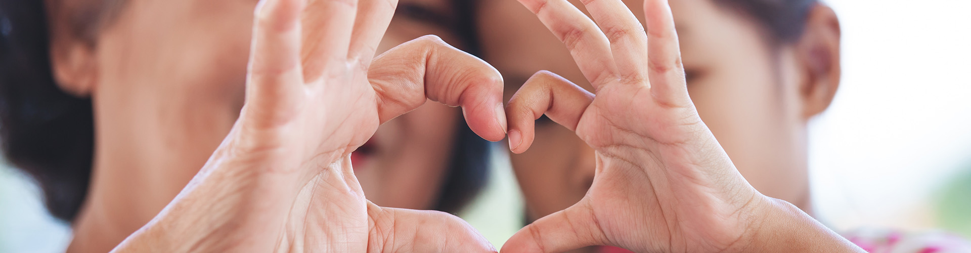 Two family members use their hands to create the shape of a heart